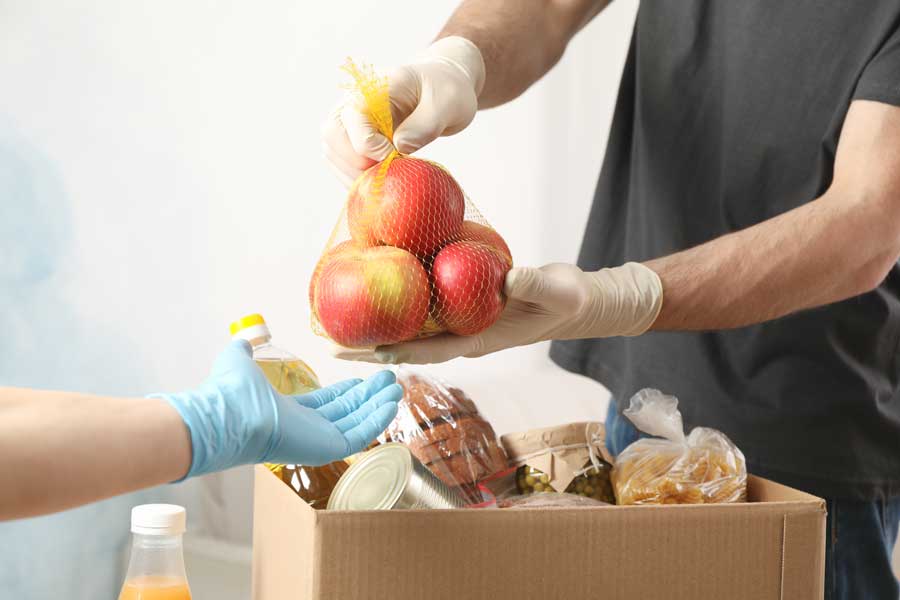 Mann reicht einen Beutel Äpfel an eine Hand im Anschitt weiter